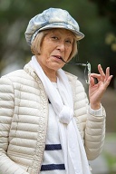 Older Japanese lady with hat and glasses smiles at the camera.