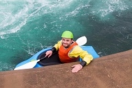 Happy teenage boy in a kayak with paddle smiling at the camera, resting against the side